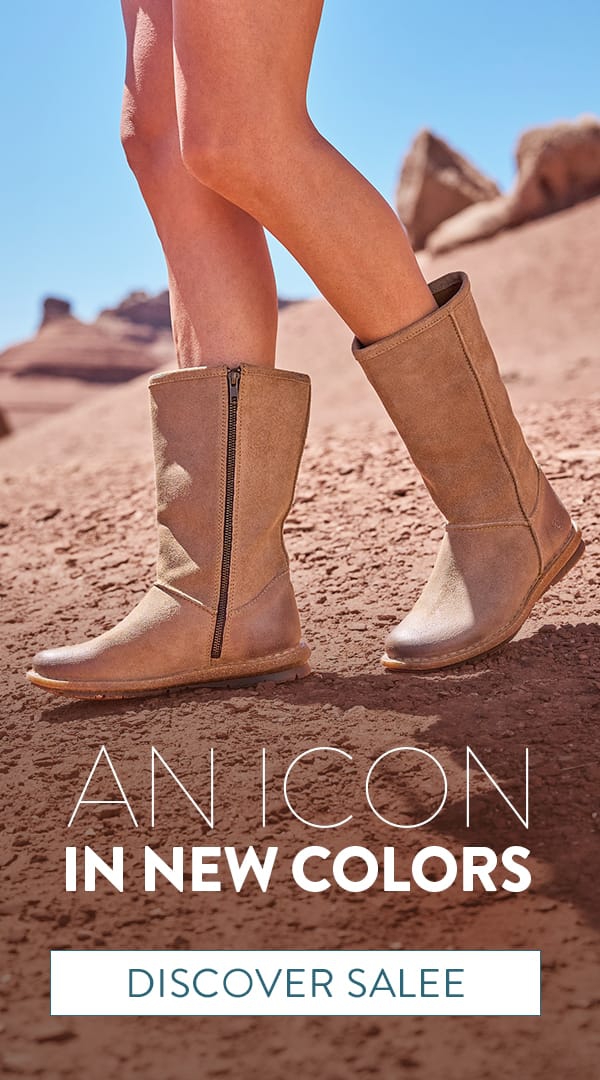 An Icon in New Colors. A woman standing in the desert wearing the Salee mid calf pull-on boots in tan suede. Discover Salee.