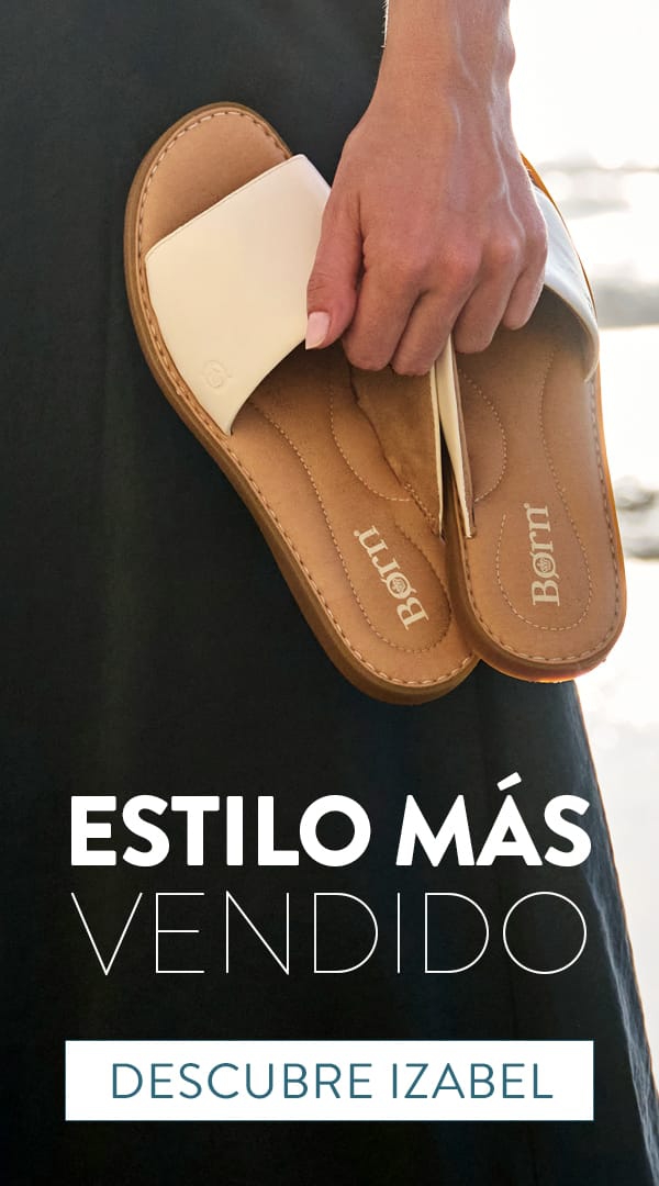 Estilo M&aacute;s Vendido. Descubre Izabel. Un modelo sosteniendo un par de sandalias tipo slide Izabel en blanco junto al oc&eacute;ano.